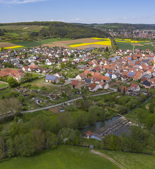 Luftbildaufnahme auf den Stadtteil Dittigheim, umrahmt von Wiesen, Feldern und Bäumen. Im Hintergrund ist die Stadt Tauberbischofsheim zu sehen. | © Tourist-Info Tauberbischofsheim
