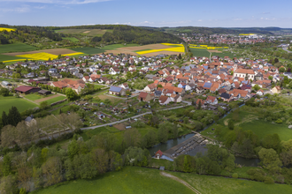 Luftbildaufnahme auf den Stadtteil Dittigheim, umrahmt von Wiesen, Feldern und Bäumen. Im Hintergrund ist die Stadt Tauberbischofsheim zu sehen. | © Tourist-Info Tauberbischofsheim