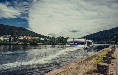 Ein weißess Ausflugsschiff welches auf einem Fluss fährt. Auf der linken Seite am Ufer sieht man eine Stadt. Neckargemünd im Odenwald. | © Touristikgemeinschaft Odenwald e.V.