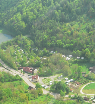 Luftbildaufnahme auf den im Tal gelegenen und mit vielen Bäumen bepflanzten Campingplatz Romantische Strasse in Creglingen-Münster. Der Hang ist bewaldet und im Hintergrund ist ein kleiner See zu sehen. | © Liebliches Taubertal