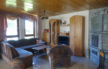 Wohnzimmer mit großer gemusterter Couch und gleichfarbigem Sessel, hohe Holzschränke und große Fenster | © Neckar-Zaber-Tourismus e.V.