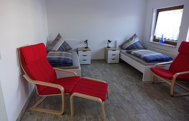 Wohn- und Schlafraum der Ferienwohnung: zwei Einzelbetten und zwei rote Sesselstühle | © Neckar-Zaber-Tourismus e.V.