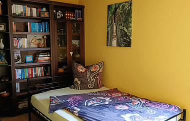 Schlafzimmer 1 mit lilafarbener Bettwäsche und einem großen Bücherschrank dahinter | © Neckar-Zaber-Tourismus e.V.