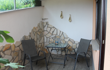 Kleine Terrasse mit zwei schwarzen Stühlen und einem quadratischen Glastisch vor einer halb mit Naturstein verkleideten Wand | © Ferienwohnung Ehrmann