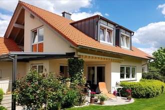 Einfamilienhaus mit rotem Ziegeldach und gepflegtem Garten bei Sonnenschein; Schlafzimmer mit Holzmöbeln und floralem Bettbezug; Wohnzimmer mit Sofa, Esstisch und moderner TV-Möbelwand. | © Familie Fuhrmann