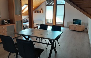 Blick in den Wohnraum der Ferienwohnung mit Esstisch, Fernseher und Sofa | © E. Hügler