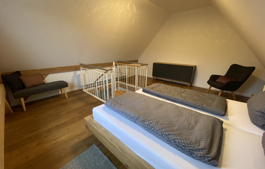 Schlafzimmer mit zwei Einzelbetten, Holzboden, Treppengeländer und Sitzgelegenheiten unter schräger Decke | © Ferienwohnung Etzl