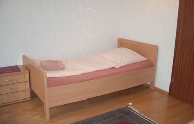 Einzelbett mit Nachttisch, grauer Teppich auf dem Boden, weiße Wände | © Neckar-Zaber-Tourismus e.V.