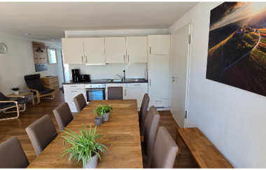 Essbereich mit großem Esstisch und vielen Stühlen, Im Hintergrund ist die Küche zu sehen | © Landgut Schellenbauer