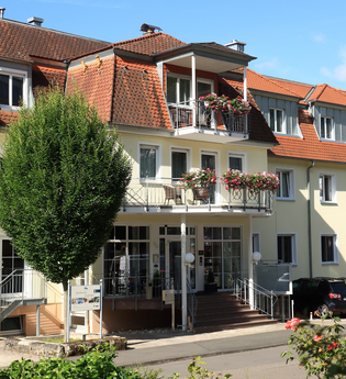 Mehrstöckiges Hotel mit gelber Fassade, roten Dachziegeln, Balkonen mit Blumen und parkenden Autos davor | © Hotel Alexa
