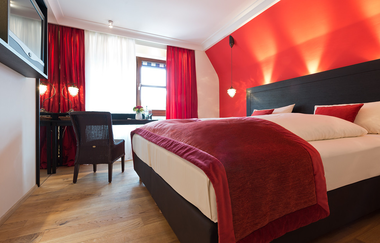 Blick in das Kabinett-Doppelzimmer "Wein-Design" im Hotel Laurentius. Die Gardinen, der Bettüberwurf und eine Wand sind rot und orange gehalten. | © Unbekannt