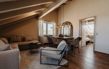 Ein großer Raum mit einem Tisch und Esszimmerstühlen. Nebenan eine Couch mit einem Sessel | © Tim Hasl