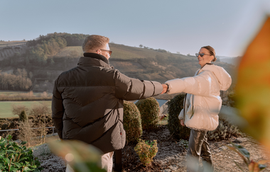 Ein Pärchen, dass Händchen hälten. Im Hintergrund sind Weinberge | © Dominik Cini