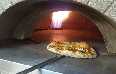 Hausgemachte Pizza mit Käse, Pilzen und Paprika im Holzofen mit sichtbarer Flamme | © Vitalhotel König