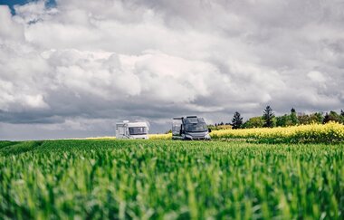 Ein grüne Wiese, dahinter fahren ein weißes und ein graues Wohnmobil. Im Hintergrund ist ein gelbes Rapsfeld. Odenwald. | © Touristikgemeinschaft Odenwald e.V