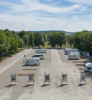 Luftaufnahme vom Stellplatz. Im Vordergrund wird der Platz durch Begrüßungstafeln abgegrenzt, Wohnmobile stehen auf dem Schotterplatz. | © Bad Mergentheim