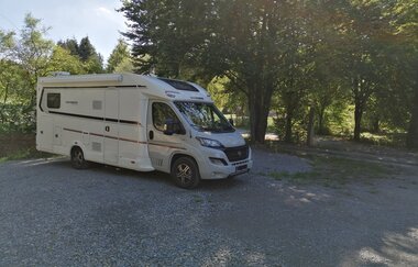 Ein weißes Wohnmobil im Schatten von Bäumen auf einem geschotterten Platz. Elztal im Odenwald. | © Erhard und Elvira Schneider "Zum Forellenbauer" GbR