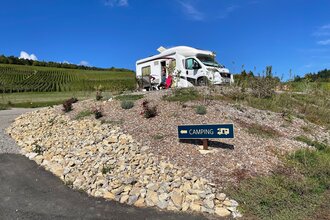 Blick auf den am Rand der Weinberge gelegenen Wohnmobilstellplatz Weingut Ehrmann.  Hier steht ein Wohnmobil. Bei schönstem Wetter und blauem Himmel genießen die im Freien sitzenden Gäste den Ausblick. | © Touristinfo Weikersheim