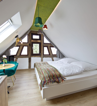 Schlafzimmer mit Doppelbett und einem kleinen Tisch mit zwei bequemen türkisfarbenen Stühlen | © Neckar-Zaber-Tourismus e.V.