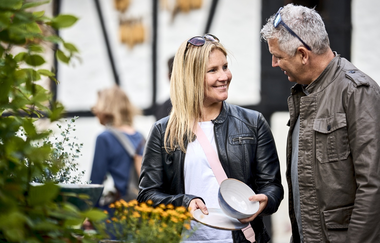 Eine Frau und ein Mann besuchen den Sindringer Töpfermarkt. Die Frau hat eine Schale und einen Teller in der Hand und lächelt den Mann an. | © Touristikgemeinschaft Hohenlohe e.V. | Stefan Leitner