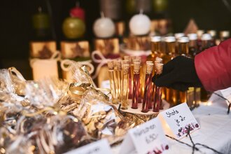 Produkte an einem Stand auf einem Weihnachtsmarkt (z.B. Shots und Gebäck). Eine Hand greift nach einem Shot im Reagenzglas. | © Touristikgemeinschaft Hohenlohe e.V. | Stefan Leitner Photography