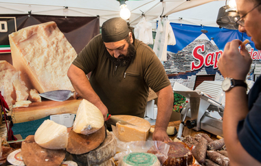 Käsehändler schneidet ein Stück Käse von einem großen Käselaib