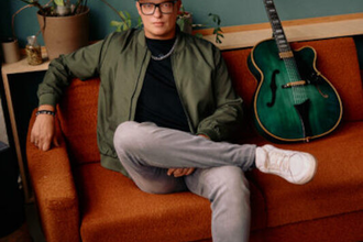 Person sitzt auf einem orangefarbenen Sofa neben einer grünen Gitarre. | © Jazzclub Schwäbisch Hall e.V.