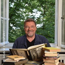 Ein Mann sitzt vor einem offenen Fenster mit Büchern auf dem Tisch. | © links im Bild