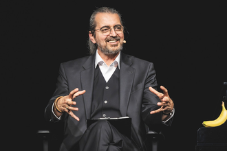 Ein Mann in einem Anzug sitzt auf einer Bühne und spricht in ein Mikrofon. | © Konzertkreis Triangel Compagnia Compostelli e.V.