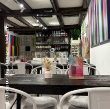 Ein stilvoll eingerichtetes Café mit modernen Kunstwerken an den Wänden und weißen Stühlen um dunkle Holztische. | © links im Bild
