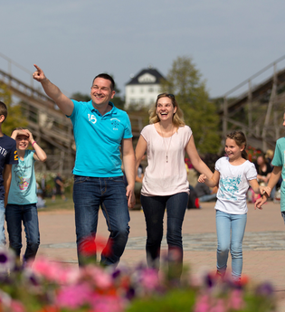 Eine Familie spaziert fröhlich in einem Freizeitpark vor einer Achterbahn. | © Erlebnispark Tripsdrill