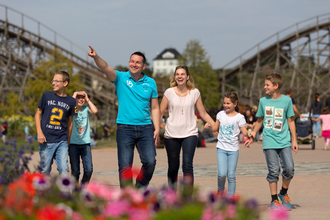 Eine Familie spaziert fröhlich in einem Freizeitpark vor einer Achterbahn. | © Erlebnispark Tripsdrill