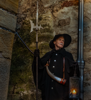 Ein Nachtwächter in historischer Kleidung mit Laterne und Hellebarde steht vor einer Steinmauer. | © Stadt Besigheim