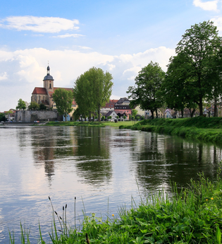 Blick auf die Regiswindiskirche bei blauem Himmel und einem umliegenden Fluss. | © Stadtverwaltung Lauffen am Neckar