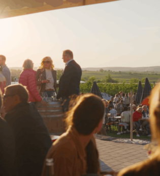 Mehrere Menschen sind in einer Hütte auf einem Weingut zu sehen. Die Sonne scheint | © Moser Burgfeld