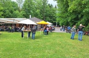 Menschen auf Wiese an Stehtischen mit Schirmen beim letzten Event