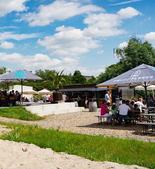 Strandkorb auf Sandfläche, Personen sitzen an Kaffeehaustischen und Biertischen | © Heuchelberg Weingärtner eG