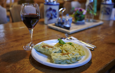 Ein Teller mit Maultaschen und Kartoffelsalat neben einem Glas Rotwein auf einem Holztisch in einer gemütlichen Besenwirtschaft | © Kraichgau-Stromberg Tourismus e.V.