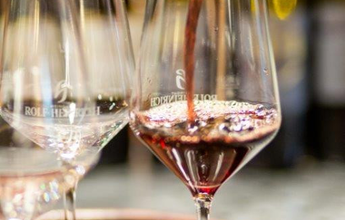 Auf einem Holztablett sind 3 Weingläser zu sehen. Eines wird gerade mit Rotwein aus einer dunklen Flasche befüllt