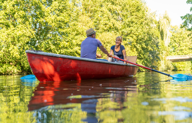 Ein Pärchen sitzt gemeinsam in einem Boot auf dem Fluss. Der Mann rudert, die Frau sitzt ihm gegenüber und lächelt. | © Björn Hänssler
