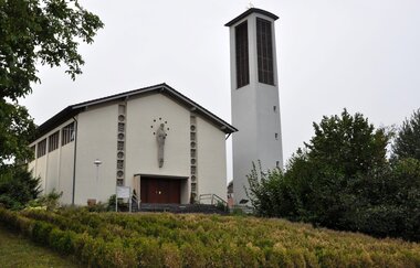 Weiße Kirche mit freistehendem Kirchturm an einem begrünten Hang