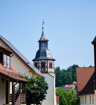 Blick durch die Gassen von Freudental mit dem markanten Kirchturm im Fachwerkstil, eingerahmt von Wohnhäusern mit roten Ziegeldächern und Solarpanels. | © Kraichgau-Stromberg Tourismus e.V.