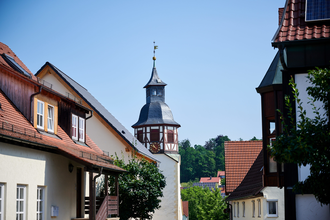 Blick durch die Gassen von Freudental mit dem markanten Kirchturm im Fachwerkstil, eingerahmt von Wohnhäusern mit roten Ziegeldächern und Solarpanels. | © Kraichgau-Stromberg Tourismus e.V.