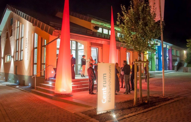 Menschen stehen vor einer mit Leuchtkörpern beleuchteten Halle bei Nacht | © Gemeinde Reichartshausen