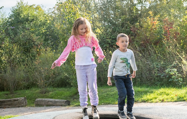 Zwei Kinder hüpfen auf im Boden eingelassenen Trampolinen
