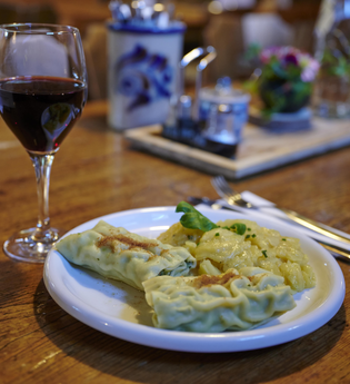 Ein Teller mit Maultaschen und Kartoffelsalat neben einem Glas Rotwein auf einem Holztisch in einer gemütlichen Besenwirtschaft | © Kraichgau-Stromberg Tourismus e.V.
