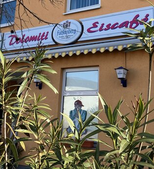 Außenansicht des Eiscafés mit Schild und grünen Pflanzen