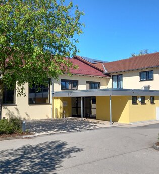 Hellgelbes zweistöckiges Gebäude mit Flachdachvorbau und Metalltreppe ins zweite OG | © Petra Natzkowski