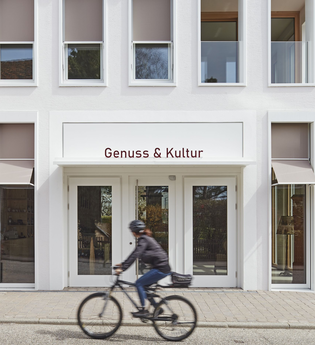 Außenansicht des weißen Gebäudes von Genuss & Kultur in Güglingen, FahrradfahrerIn davor | © NZT