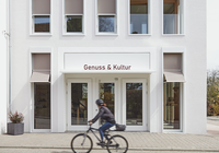 Außenansicht des weißen Gebäudes von Genuss & Kultur in Güglingen, FahrradfahrerIn davor | © NZT